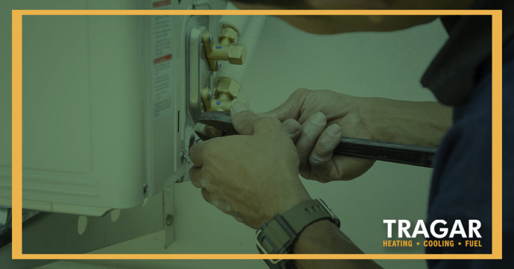 Person using tools to install or repair an HVAC unit, with the Tragar Heating, Cooling, and Fuel logo visible.