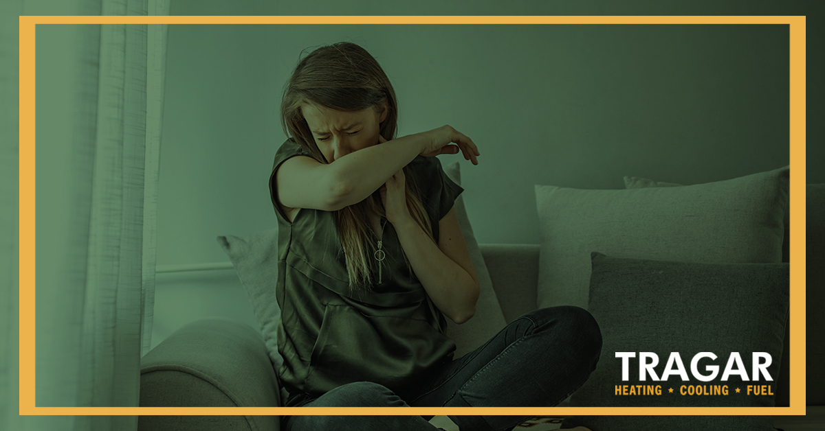 Woman on the couch coughing into her arm.