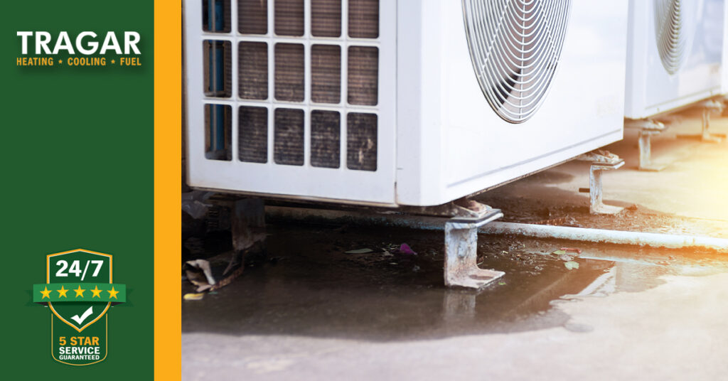 An outdoor air conditioning unit on a concrete surface with water puddles beneath. Tragar logo on the left side, advertising heating, cooling, and fuel services.