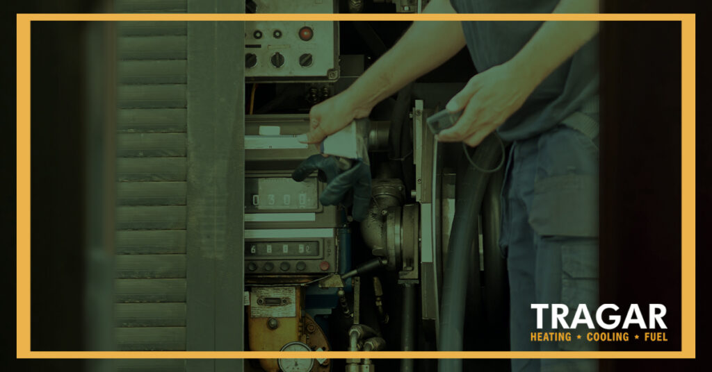 Person adjusting controls on HVAC equipment, wearing gloves. The image features the Tragar logo in one corner.