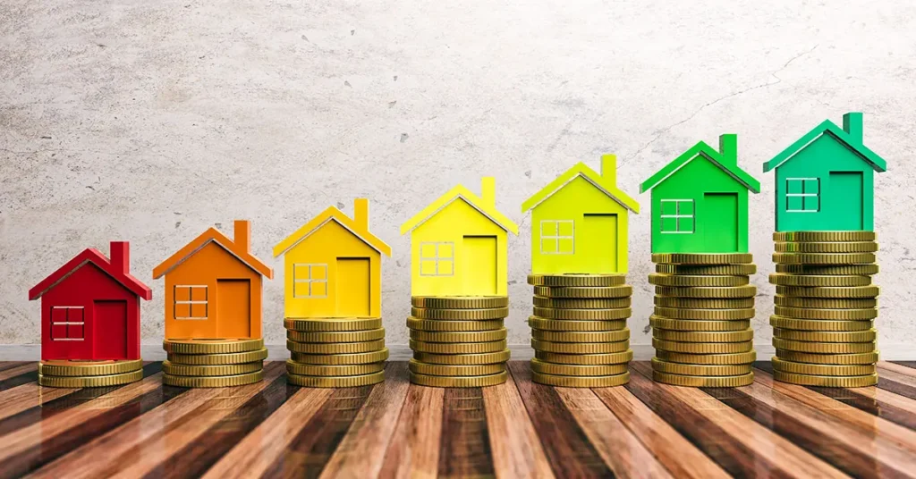 Colorful house models perched on stacks of coins, each in ascending heights on a wooden surface, capture the essence of investment growth. This setup symbolizes the increasing property value and tells a vivid story about us.