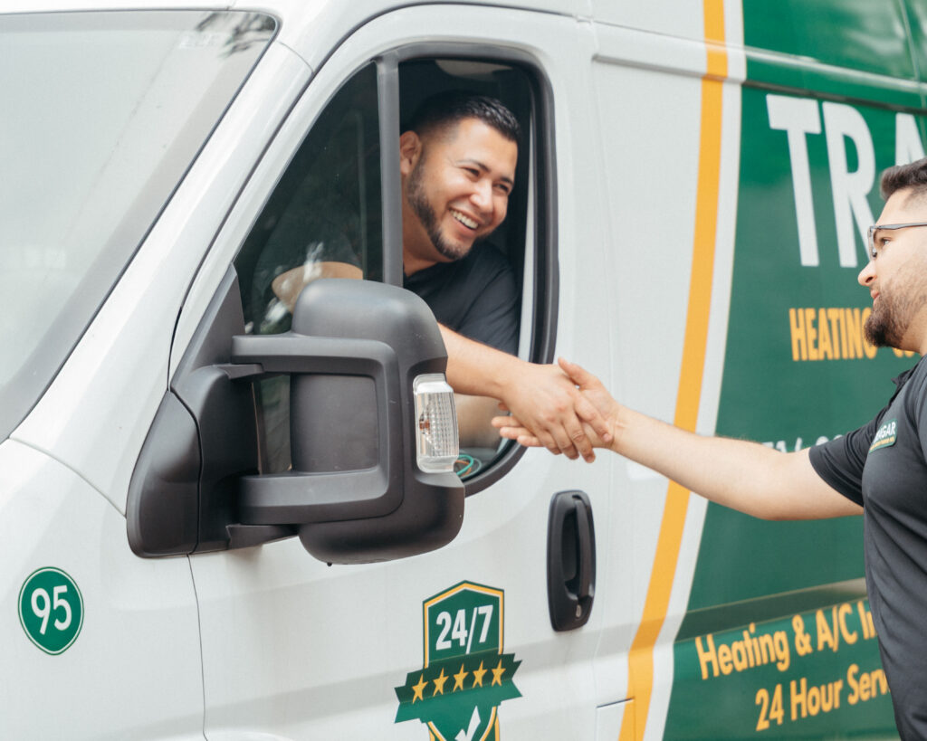 Two men shake hands by a white service van with green and yellow branding. One man is inside the van, smiling, while the other stands outside—highlighting a positive moment that reflects new careers and job opportunities within the company.