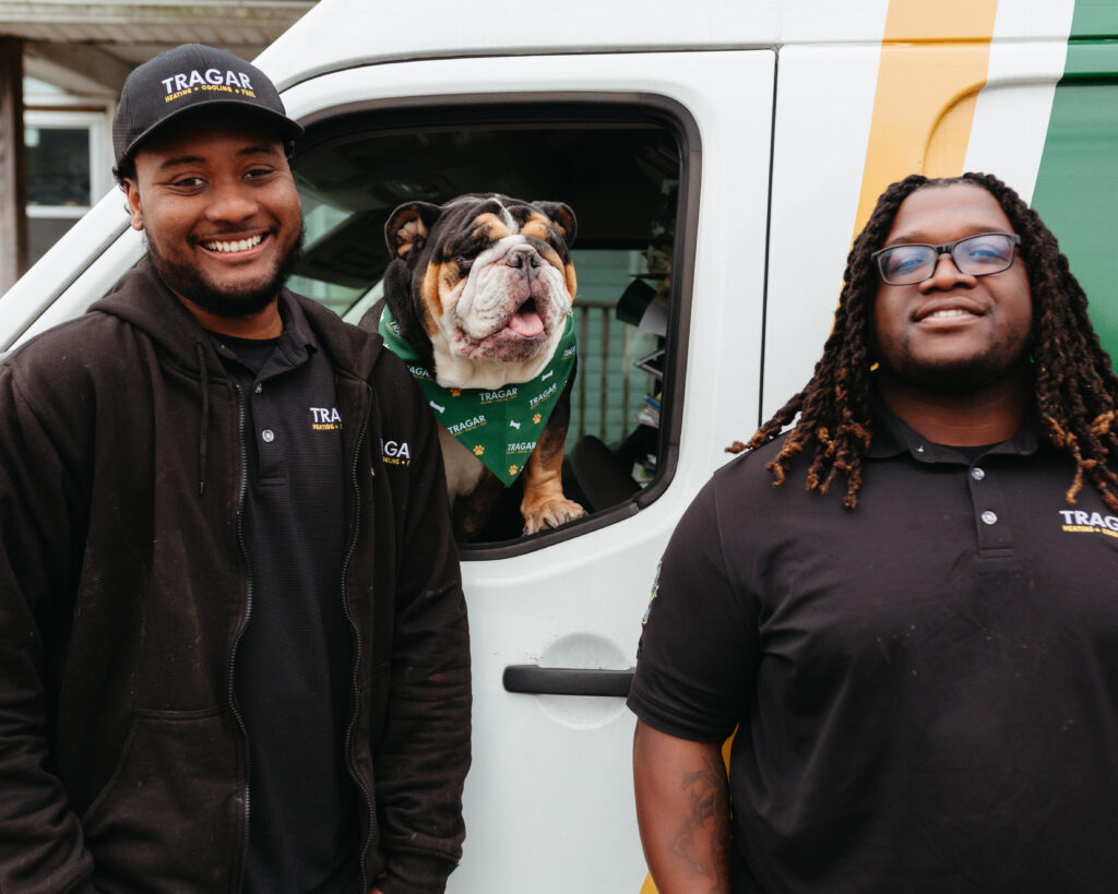 Two men in black company uniforms stand next to a van with a bulldog wearing a green bandana sitting in the driver’s seat window, proudly representing a team that’s always hiring and offering rewarding careers.