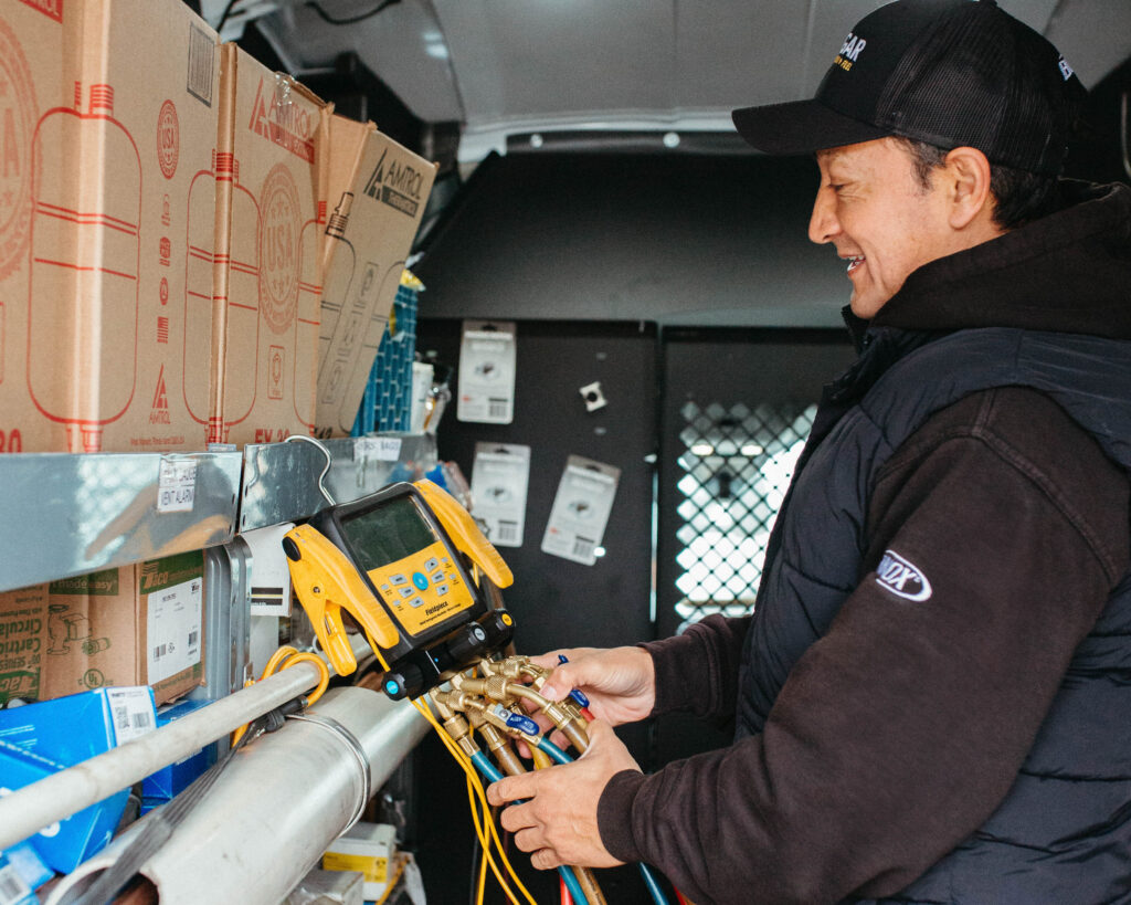 A person in a black jacket uses a yellow HVAC diagnostic tool connected to pipes inside a service van filled with boxes and equipment, showcasing the hands-on skills essential for many rewarding HVAC careers.